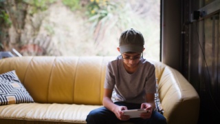 Boy sitting on sofa near window texting on mobile phone