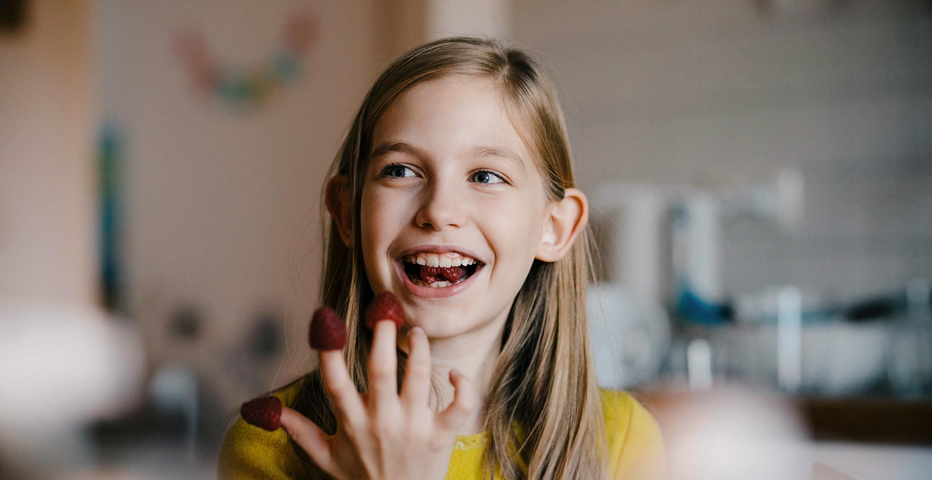 Girl sitting at home smiling and eating raspberries