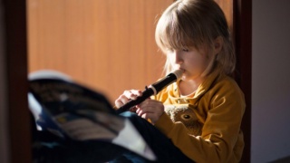 Child (6-7) sitting in a doorway at home, practising playing the recorder