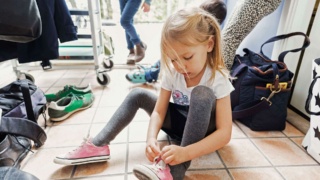 Young girl tying her shoes whilst sitting on the floor