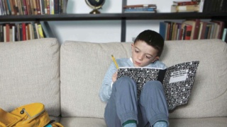 Boy with Noonan Syndrome doing schoolwork on a sofa