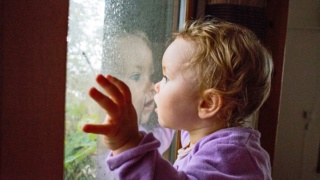 Young girl (2-3) watching the rain with face up to the window